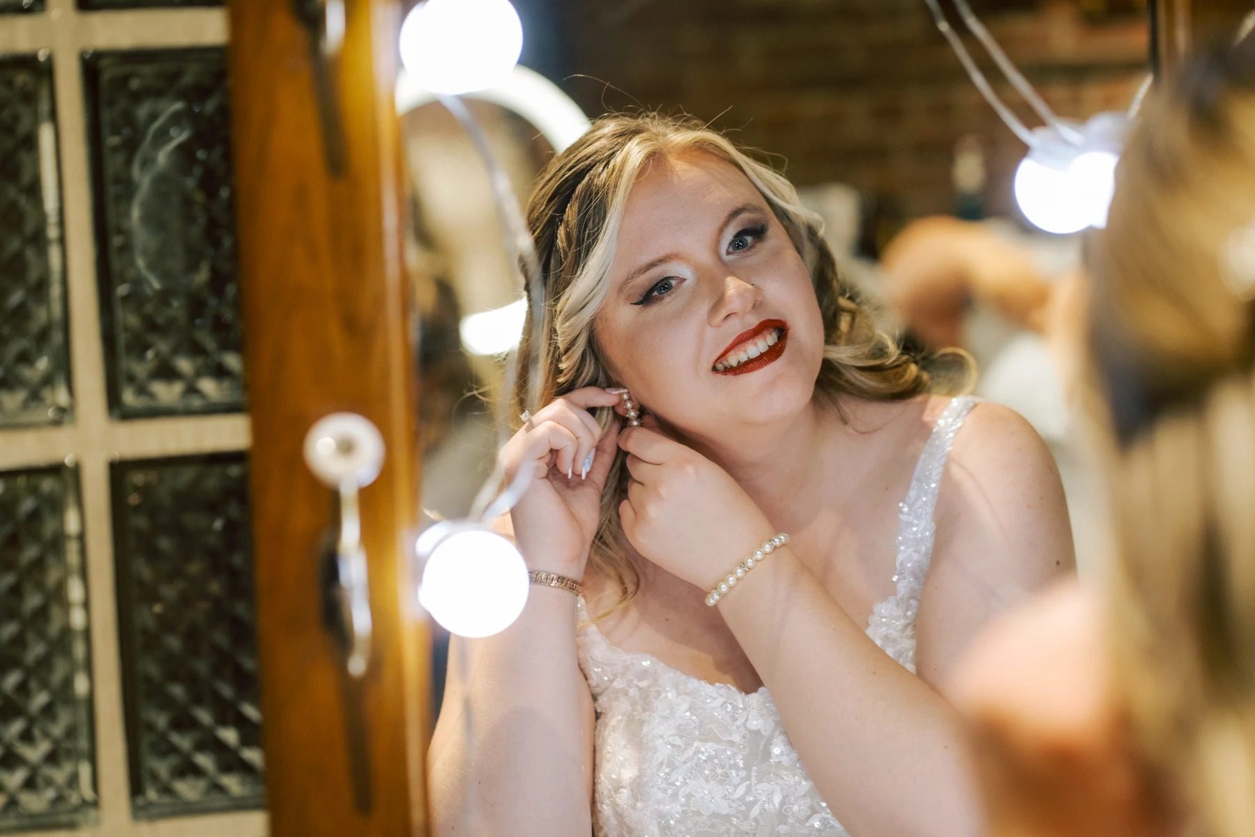 Bride adjusting her earring while looking at her reflection in a vanity mirror. — Wedding at Dramatic Hall, peekskil, ny
