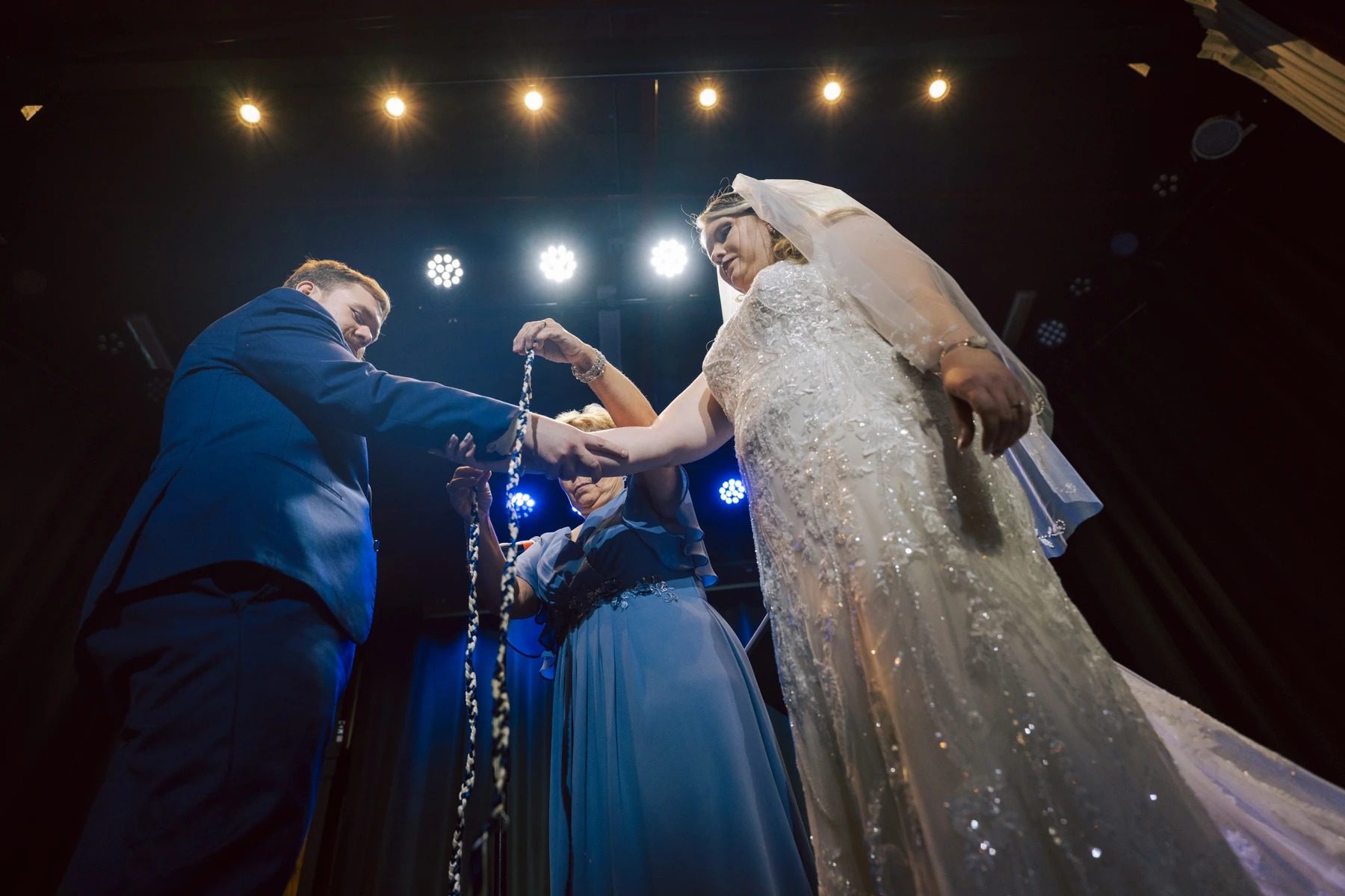 Bride and groom exchanging vows or rings with officiant during ceremony under stage lights. — Wedding at Dramatic Hall, peekskil, ny