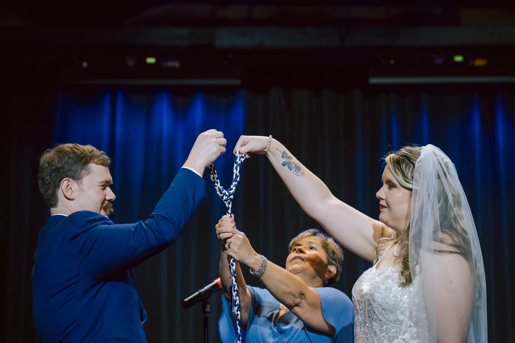 Bride and groom hold up a decorative chain together while an officiant stands between them during the ceremony. — Wedding at Dramatic Hall, peekskil, ny