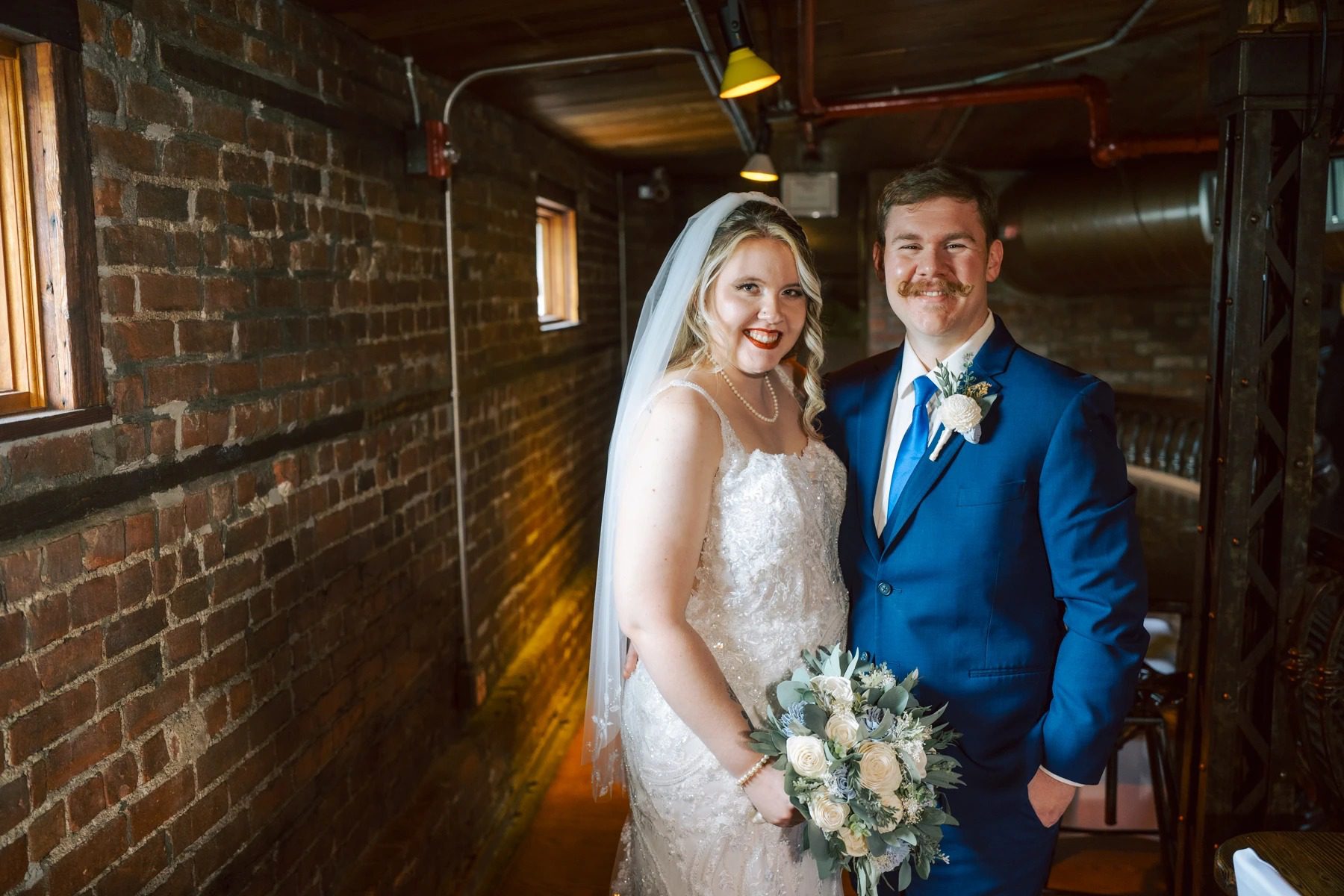 Bride and groom standing together in an industrial corridor, holding her bouquet and smiling at the camera. — Wedding at Dramatic Hall, peekskil, ny