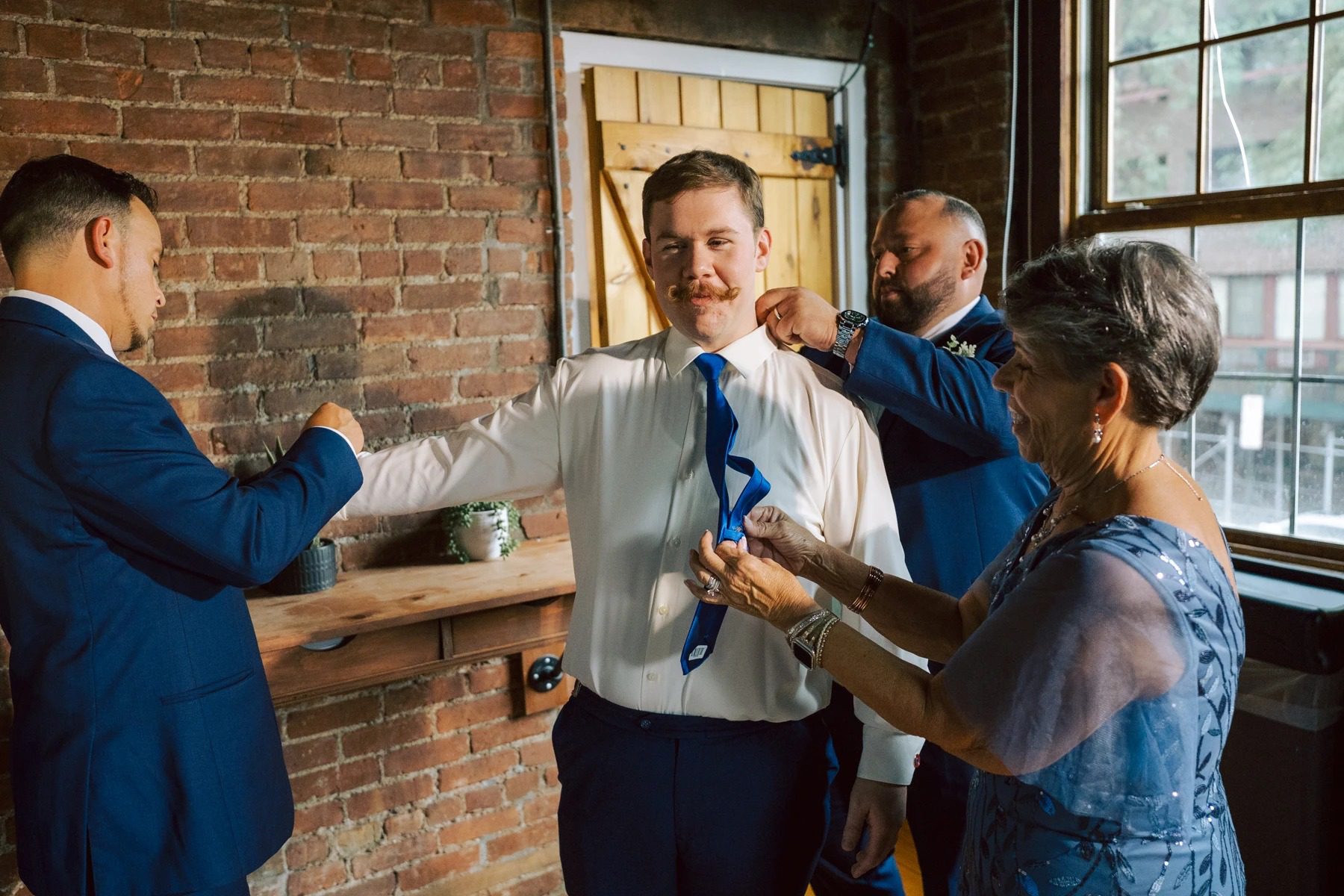 Groom being dressed by family members who are fastening his tie and adjusting his jacket. — Wedding at Dramatic Hall, peekskil, ny