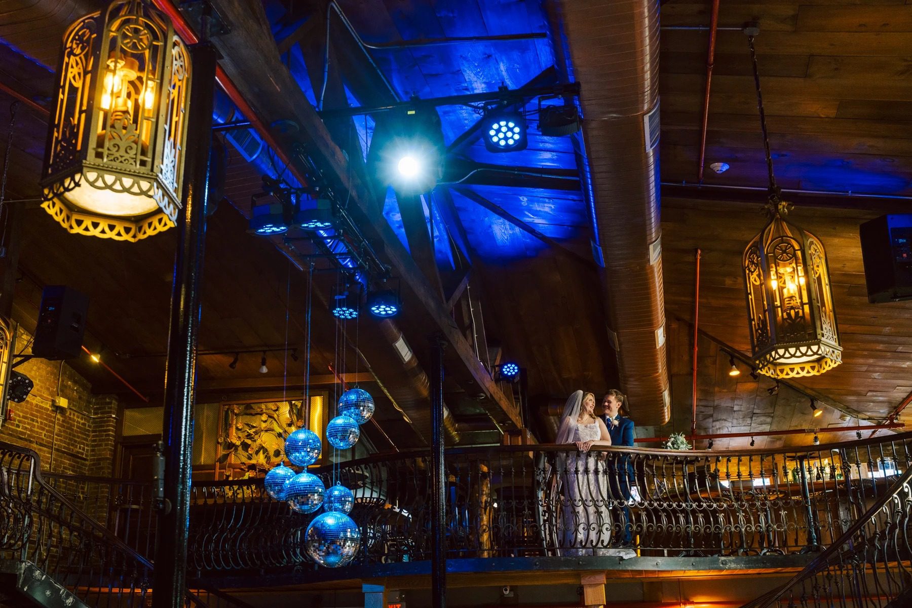 Guests mingling on a multi-level venue interior at night, illuminated by decorative lanterns and blue accent lighting. — Wedding at Dramatic Hall, peekskil, ny