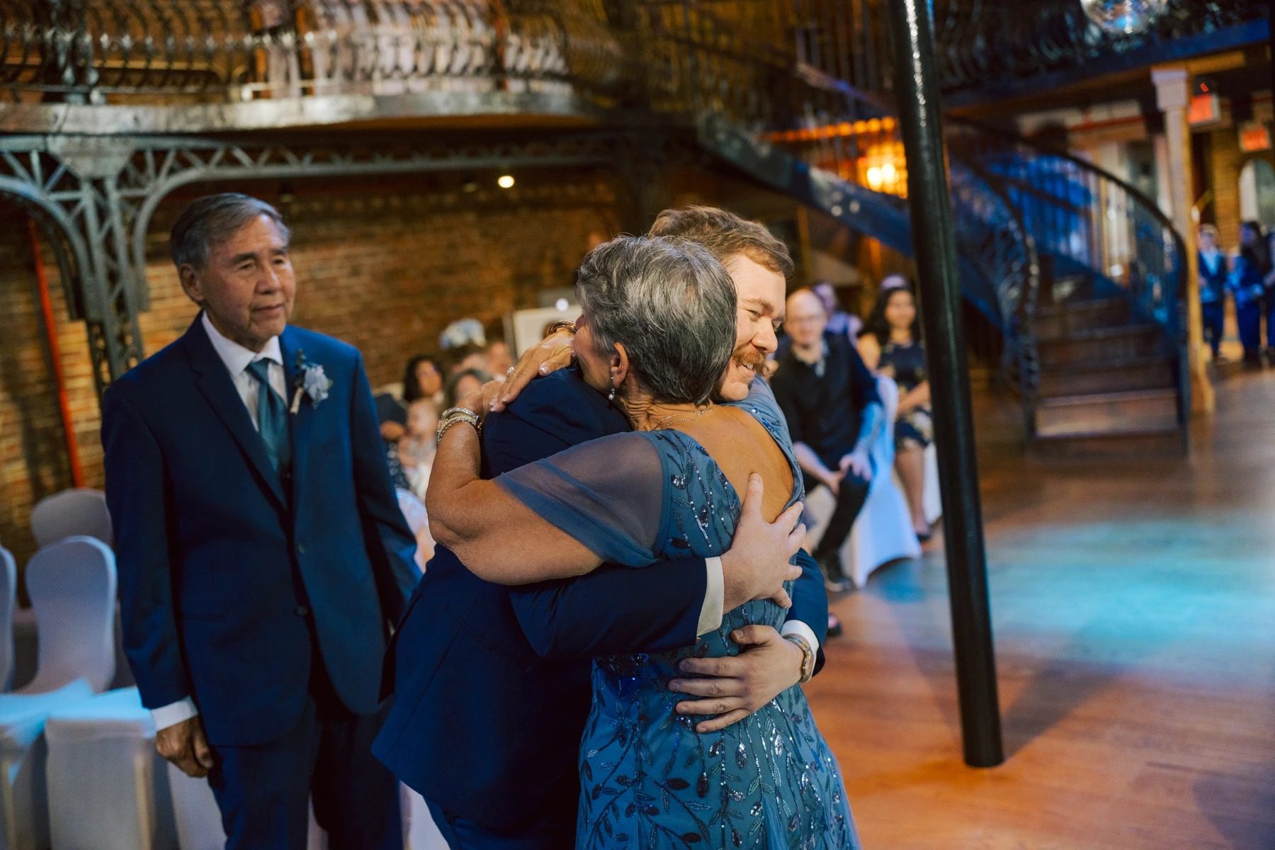 Mother and son embrace during wedding reception while guests watch from the dance floor. — Wedding at Dramatic Hall, peekskil, ny