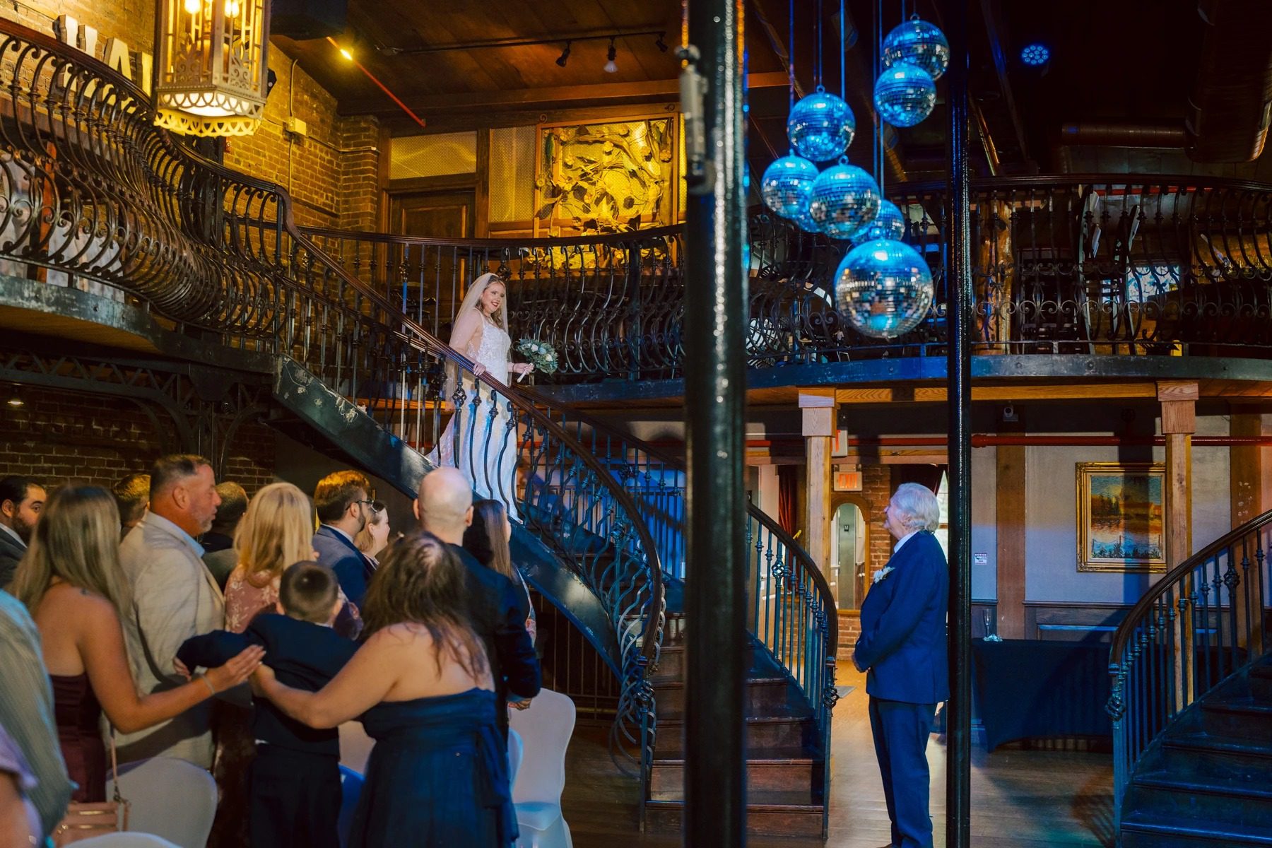 Wedding guests mingling and celebrating on a multi-level indoor venue with blue decorative spheres hanging overhead. — Wedding at Dramatic Hall, peekskil, ny