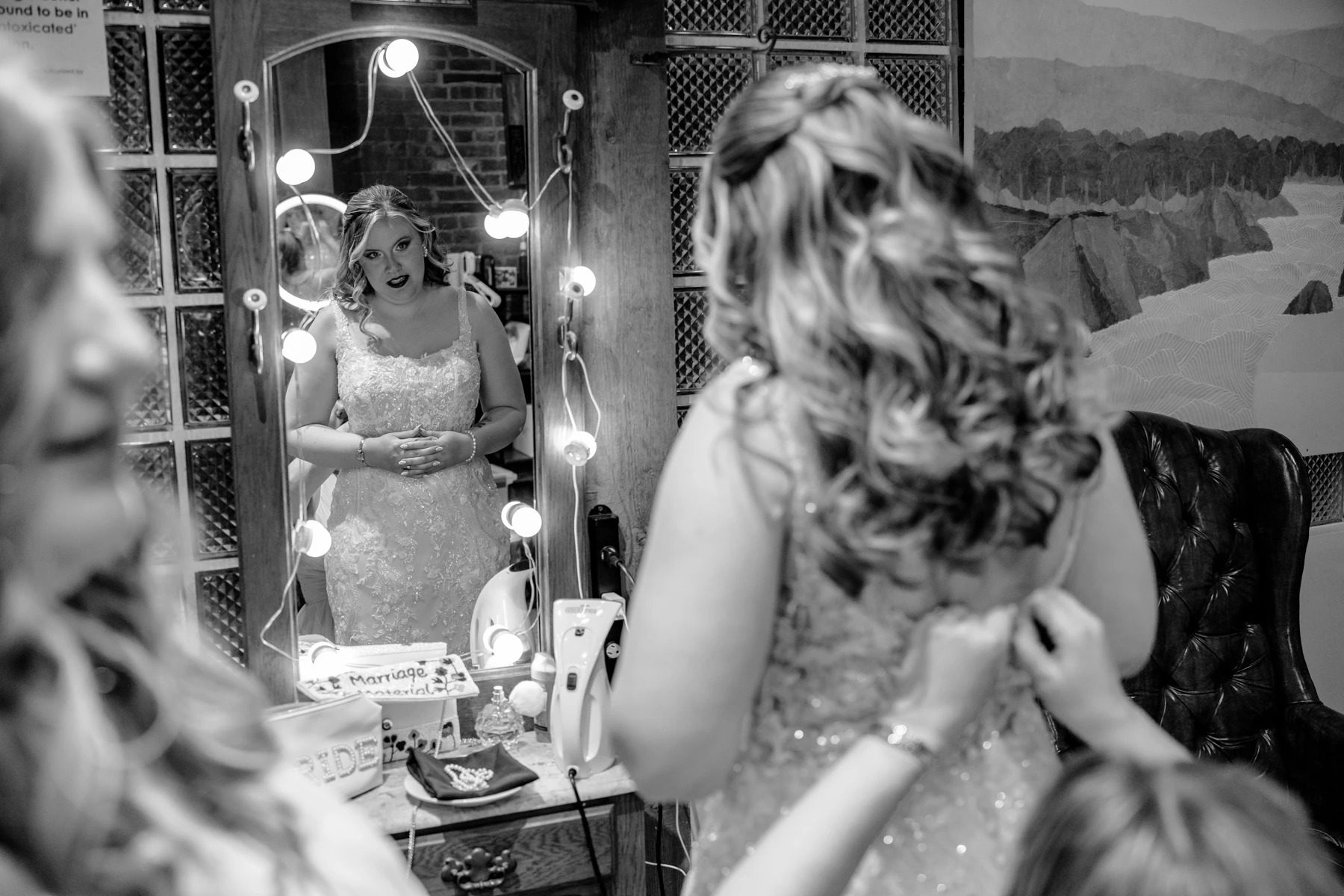 Woman in sequined dress adjusting her hair while looking in a lighted vanity mirror. — Wedding at Dramatic Hall, peekskil, ny